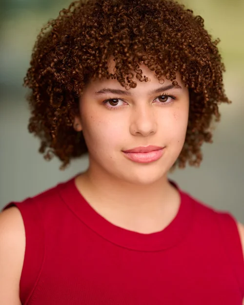 Talent headshot with short curly hair and a red sleeveless top