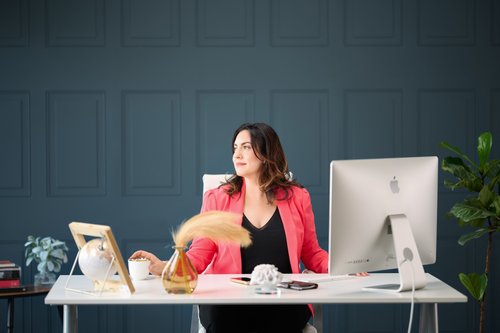 Branding portrait in a pink blazer at a desk with a computer