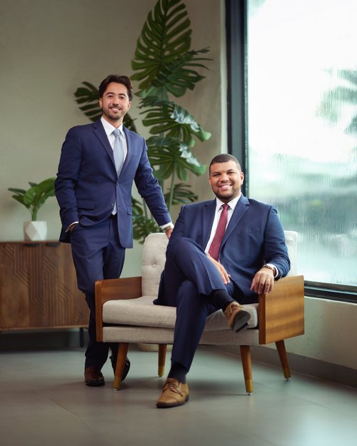 Two-person business portrait with a wooden armchair beside a window