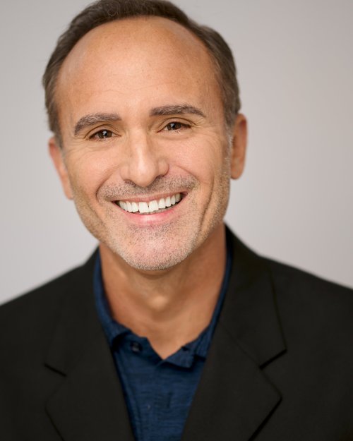 Smiling talent headshot in a black blazer and blue shirt
