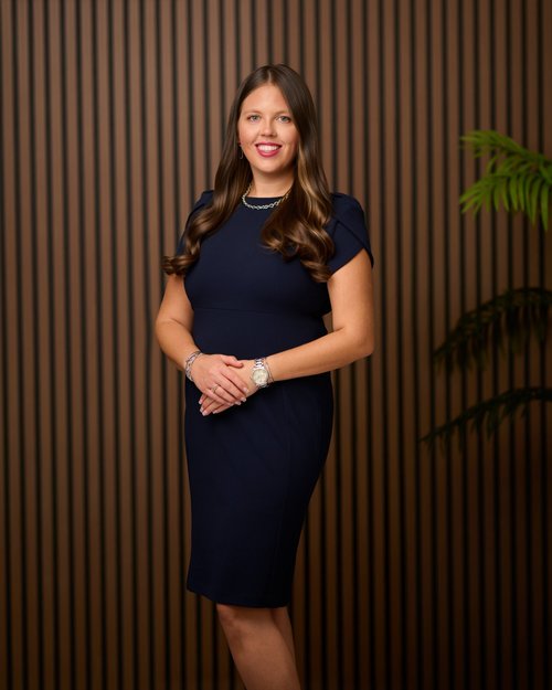Professional portrait in a navy dress beside a wood slat wall