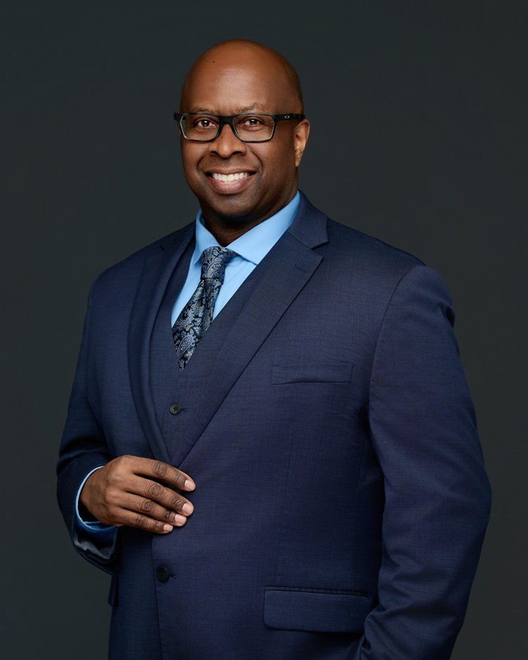 Studio portrait of a Black legal professional in a navy suit.