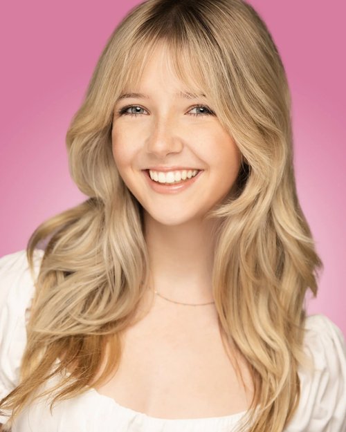Smiling talent headshot with long blonde hair against a pink backdrop