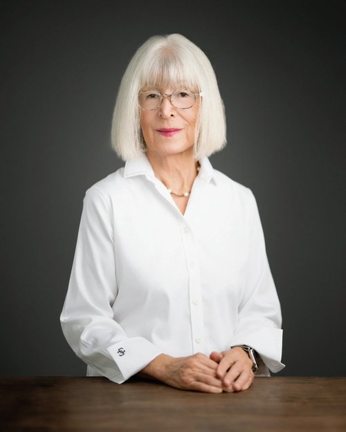 Studio portrait in a white blouse, seated at a wooden table against a dark backdrop