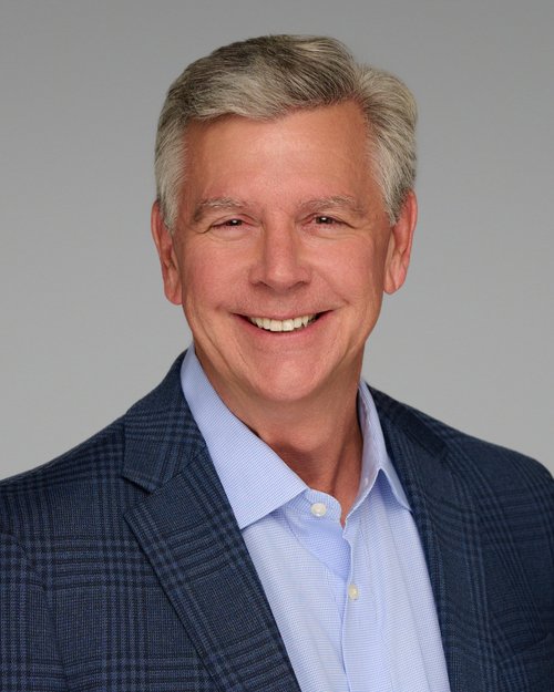 Smiling headshot in a navy checked blazer and light blue shirt