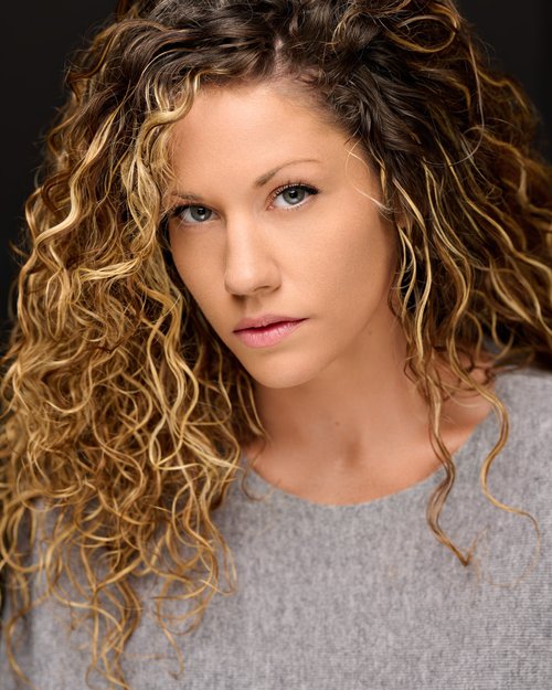 Talent headshot with curly blonde hair and a gray top