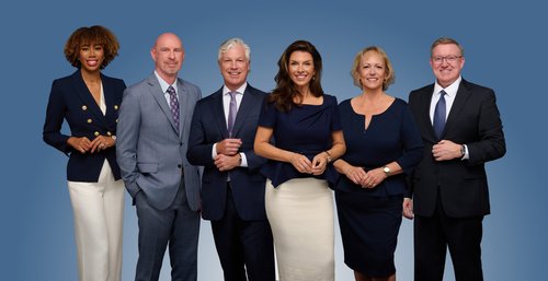 Six-person team portrait in coordinated business attire against a blue backdrop
