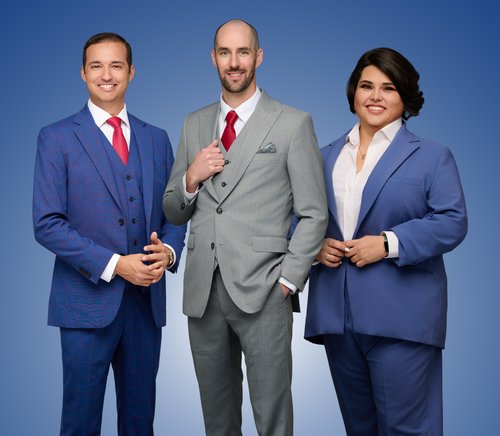 Three-person team portrait in blue and gray suits against a blue backdrop