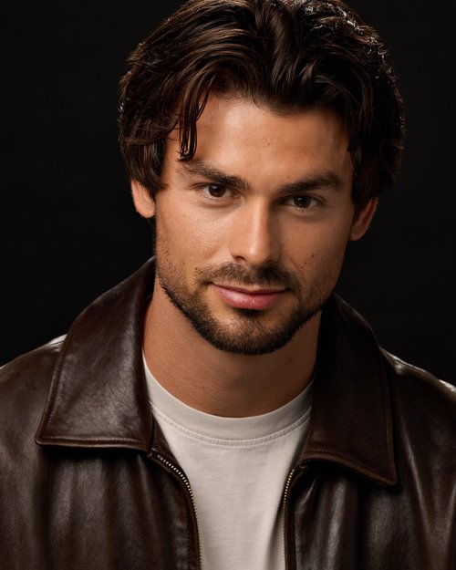 Talent portrait in a brown leather jacket and white T-shirt against a dark backdrop