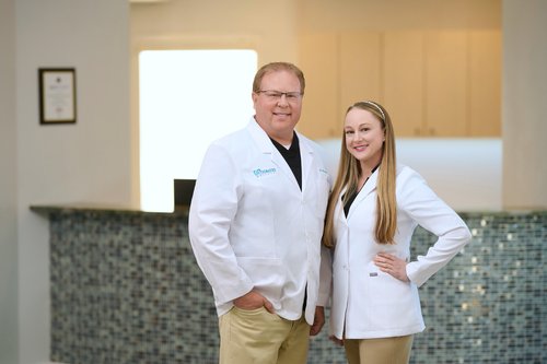 Two-person portrait in white medical coats beside a reception counter