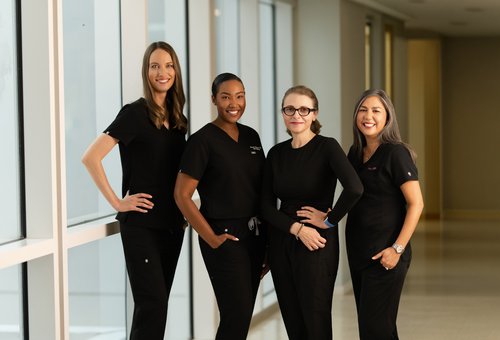 Four-person team portrait in black scrubs beside hallway windows