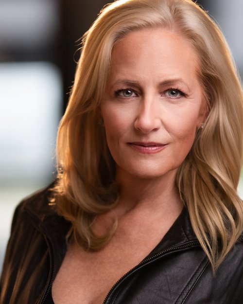 Talent headshot with blonde hair and a black zip-front top