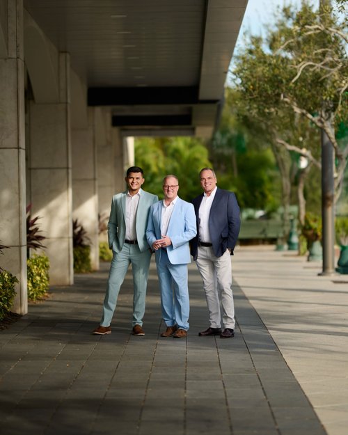 Three-person outdoor team portrait in suits beneath a covered walkway