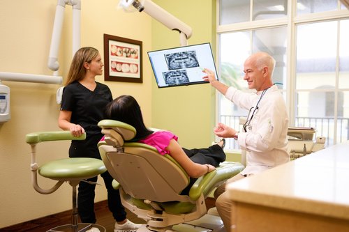 Dental consultation photograph with a patient, dental chair and X-ray display