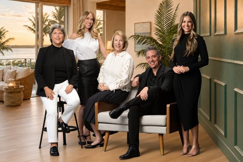 Five-person team portrait arranged around a chair in a furnished interior