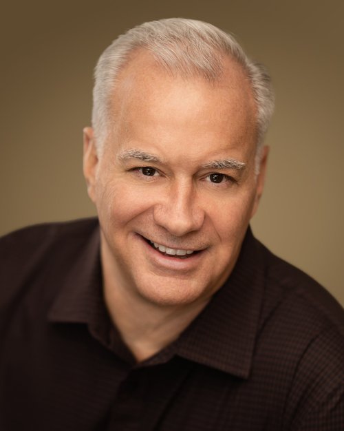 Smiling talent headshot in a dark collared shirt against a warm backdrop