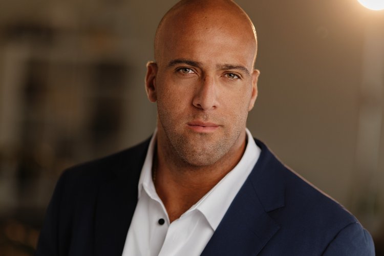 Actor headshot of a man in a navy jacket.
