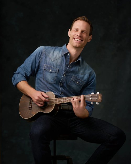 Studio portrait playing an acoustic guitar against a dark backdrop