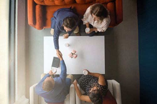 Overhead branding photograph of four people greeting one another around a coffee table