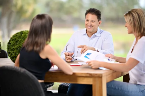 Three people discussing documents around a wooden table