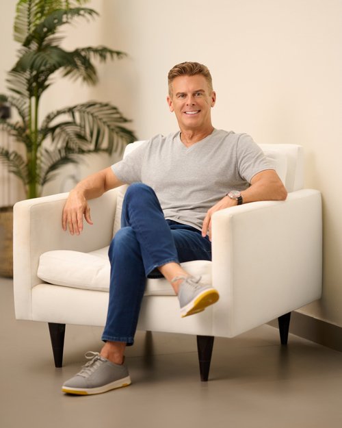 Casual portrait in a gray T-shirt and jeans, seated in a cream armchair